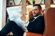 © GVS - Confident young businessman reading newspaper and latest news while sitting in armchair