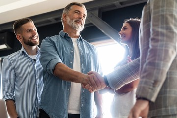 Canvas Print - Welcome to our team! Business men in smart casual wear shaking hands while working in the creative office.