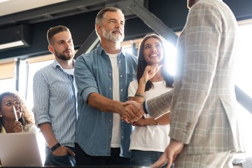 Canvas Print - Welcome to our team! Business men in smart casual wear shaking hands while working in the creative office.