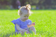 © Igor Butseroga - Cute little girl sits on the green grass, outdoors, summer time, blurred background