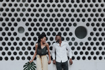 Gorgeous black couple in love look into each other and smile on geometric background. engagement photo shoot. amazing stylish black models