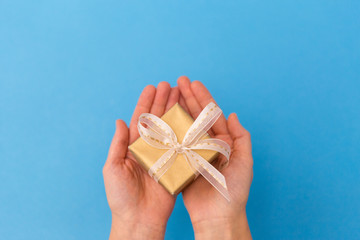 holiday, presents and greetings concept - hands holding small christmas gift box on blue background