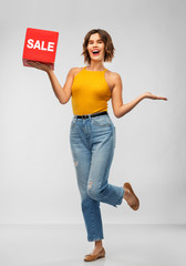 Wall Mural - shopping and people concept - happy smiling young woman in mustard yellow top and jeans with sale sign posing over grey background