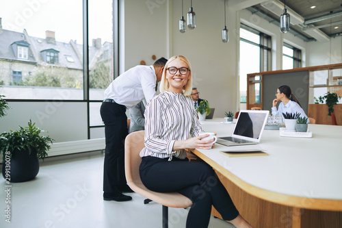 Cuadros en Lienzo Smiling young businesswoman sitting in a boardroom drinking coff