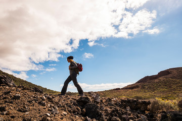 Wall Mural - Expedition concept with woman walking on the rocks in trekking activity - outdoor leisure active people - scenic place with curved mountains horizon and blue sky with clouds