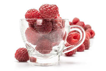 Wall Mural - Lot of whole fresh crimson raspberry with glass cup isolated on white background