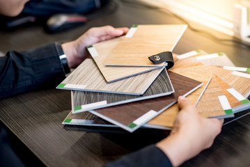 Male architect or interior designer holding wooden color swatch choosing wood material for housing project. Sample of wood laminated chipboard for furniture design. Architecture and construction.