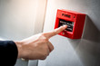 © zephyr_p - Male hand pointing at red fire alarm switch on concrete wall in office building. Industrial fire warning system equipment for emergency.