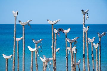 Wooden sculpture of a group of seagulls with blue sea and sandy beach in the background