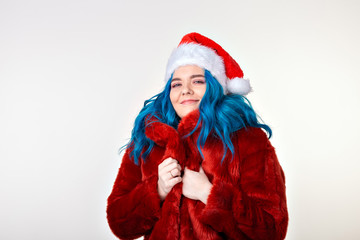 Canvas Print - Studio fashion portrait of young woman with blue hair in stylish winter fluffy red coat and christmas santa hat posing on white background.