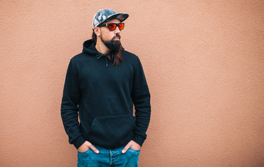 Wall Mural - City portrait of handsome hipster man with beard wearing black blank hoodie or hoody with space for your logo or design. Mockup for print