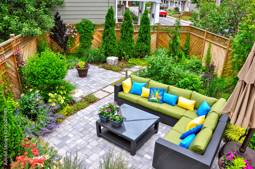 A beautiful small, urban backyard garden featuring a tumbled paver patio, flagstone stepping stones, and a variety of trees, shrubs and perennials add colour and year round interest.  - obrazy, fototapety, plakaty 