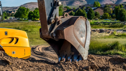 Wall Mural - Panorama Metal arm and bucket of a yellow excavator digging soil at a construction site