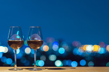 Two glasses of Rose wine with bokeh city colorful light from rooftop building.