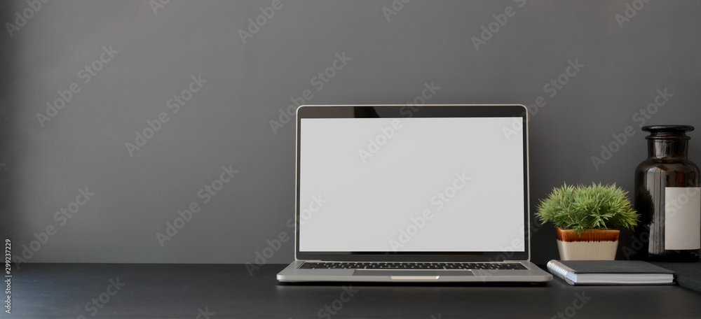 Open blank screen laptop computer in dark trendy workplace with copy space - obrazy, fototapety, plakaty 