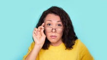 Funny Shocked Face. Frames Trying Eyeglasses. Girl Holding Glasses Standing On Turquoise Background, Concept: Poor Eyesight.