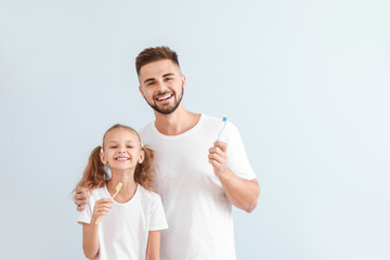 Portrait of father and his little daughter with toothbrushes on light background