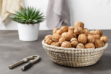 Walnuts and nut kernels in a basket with a nutcreacker on a concrete kitchen table, light-filled space