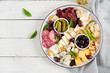 Antipasto platter with basturma, salami, blue cheese, nuts, pickles and olives on a white wooden background. Top view, overhead