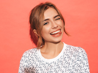 Young beautiful woman looking at camera. Trendy girl in casual summer shirt clothes with natural makeup. Positive female smiling. Funny model posing near pink wall in studio.Shows tongue and winks