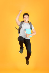 Wall Mural - Excited young Asian man jumping with a backpack on the an orange background