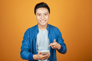 Wall Mural - Asian man happy to see what in the smartphone on isolated orange background.