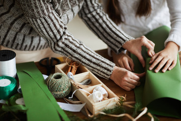 Close-up of family of two decorating gift box with green paper together at the table for Christmas