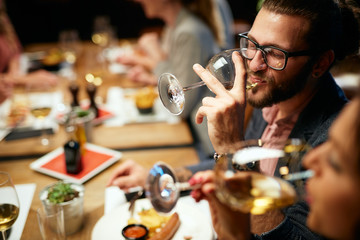 Sticker - Handsome caucasian bearded hipster man with eyeglasses drinking wine while sitting with his friends in restaurant.