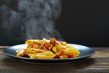 Wall Mural - Hot pasta with steaming on wooden table and dark background. Pasta served with spicy tomato sauce on wood table on black background. Hot food concept. 