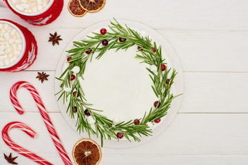 top view of candy canes, two cups of cocoa and christmas pie with icing on white wooden table