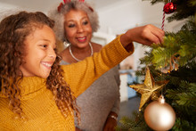 Grandmother And Granddaughter Decorating Christmas Tree At Home Together