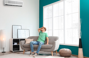 Wall Mural - Young man suffering from heat under broken air conditioner at home