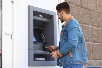 Young man using modern cash machine outdoors