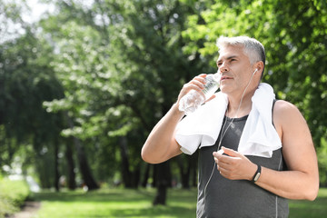 Wall Mural - Handsome mature man with bottle of water in park, space for text. Healthy lifestyle