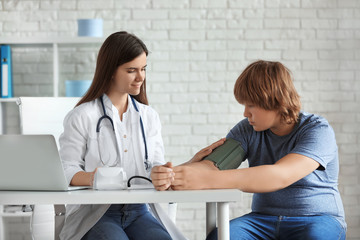 Female doctor checking overweight boy's blood pressure in clinic