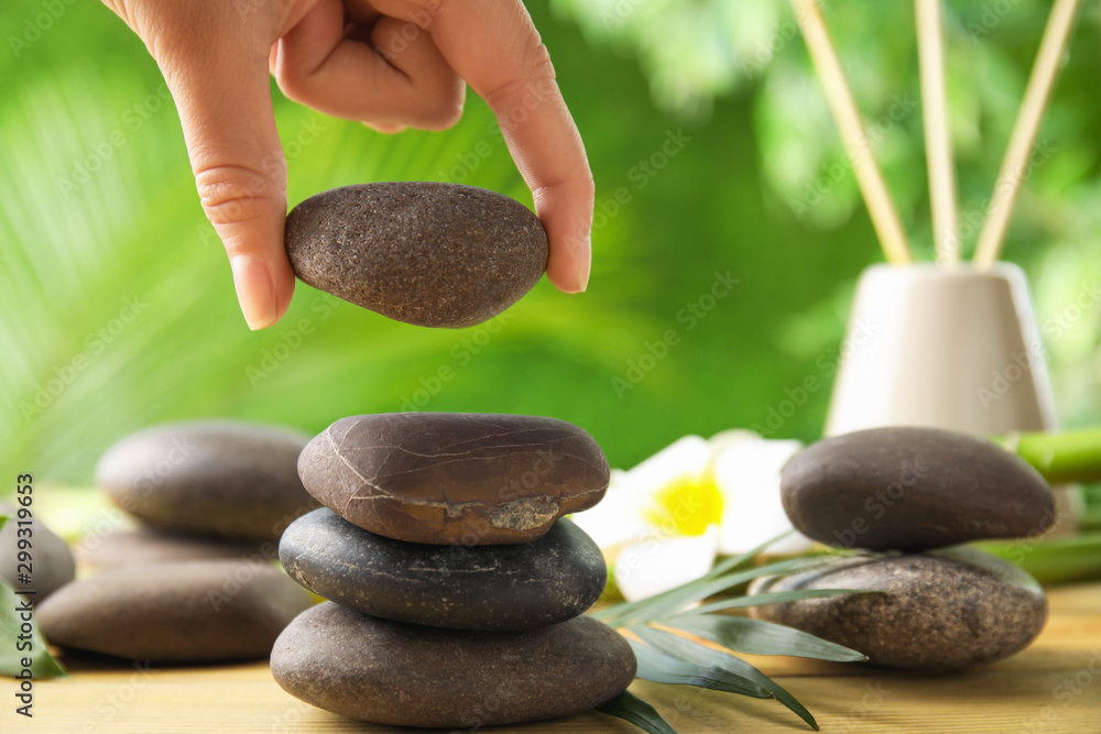 Woman stacking stones on table against blurred background, closeup. Zen concept - obrazy, fototapety, plakaty 