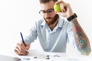 Image of serious young man holding tennis ball while working in office