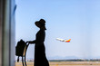 © Imaging L - Tourist is standing in airport and looking at aircraft flight through window.
