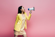 © LIGHTFIELD STUDIOS - side view of asian woman in yellow outfit screaming in megaphone isolated on pink