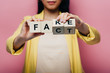 © LIGHTFIELD STUDIOS - cropped view of asian woman holding wooden cubes with fake and fact lettering isolated on pink