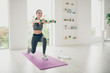 © deagreez - Full length photo of joyful active athlete woman holding strong dumbbells doing gymnastics exercise standing on purple mat in house like gym