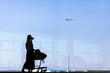 © Imaging L - Tourist is standing in airport and looking at aircraft flight through window.