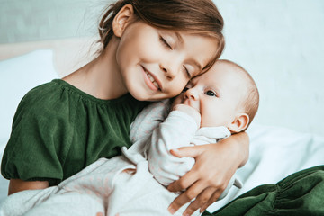 Wall Mural - adorable child smiling with closed eyes while holding little sister