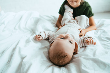 Wall Mural - cropped view of smiling kid touching infant lying on white bedding