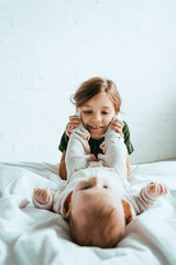Wall Mural - selective focus of happy child touching legs of adorable baby lying on white bedding