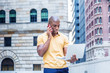 © Alexander Image - Working anywhere. Young African American Business Man working in New York City, wearing yellow short sleeve shirt, standing outside office building, talking on cell phone, working on laptop computer..