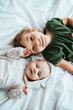 top view of smiling child looking at camera while lying on white bedding near little sister