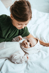 Wall Mural - adorable child looking at cute little sister lying on white bedding