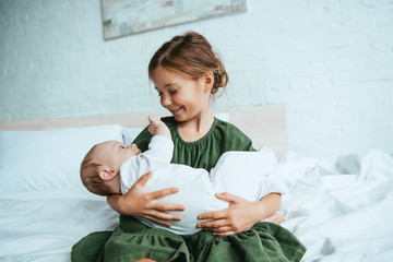 Wall Mural - happy child holding cute little sister while sitting on white bedding