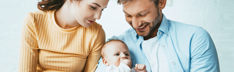 Wall Mural - panoramic shot of happy parents smiling while looking at cute infant